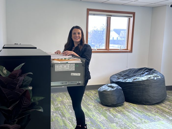 A woman sorts through documents in a large filing cabinet near a window