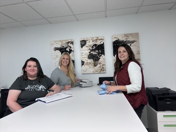 Three women sit at a desk and smile at Illinois Registered Office