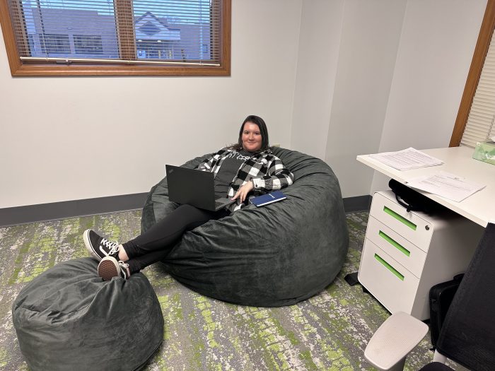 A woman lounges on a beanbag chair while typing on a laptop.