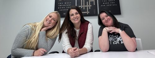 Three employees sitting at a table smiling.